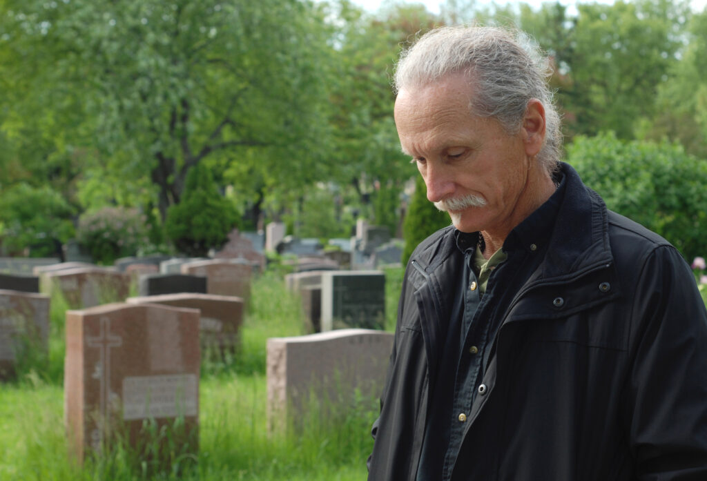 Sorrowful man standing in cemetery with head bowed