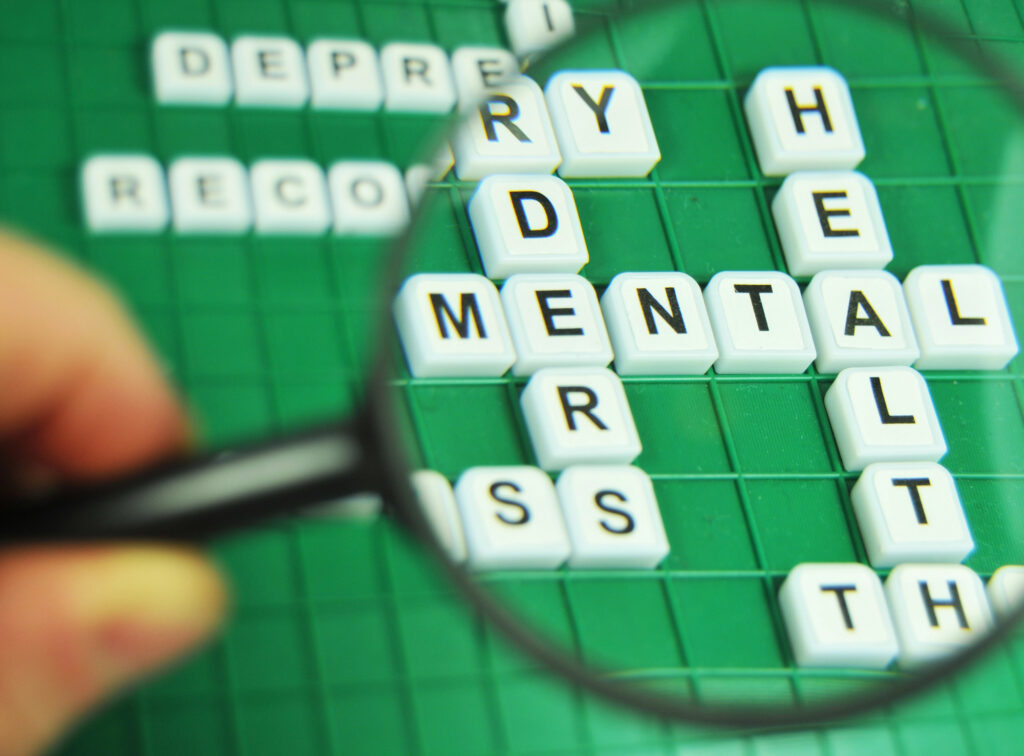 Magnifying glass enlarging a crossword puzzle with mental health as an answer 