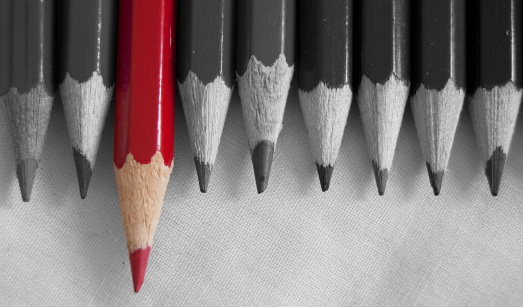 Red pencil amongst a row of pencils in black and white.