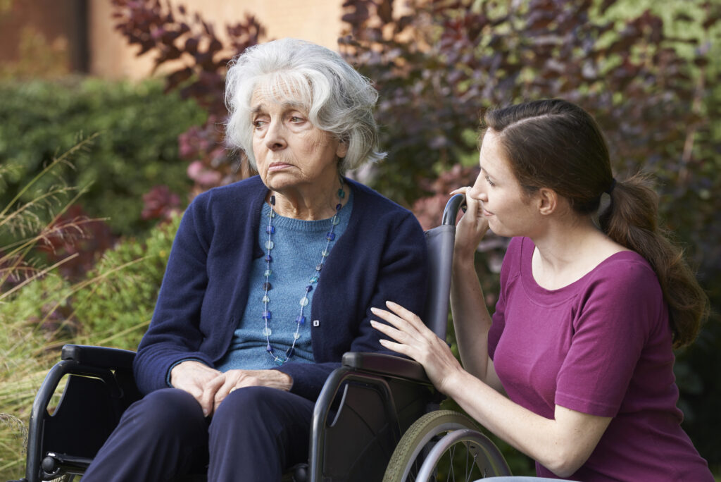 caregiver kneeling down smiling at a geriatric woman who is distraught