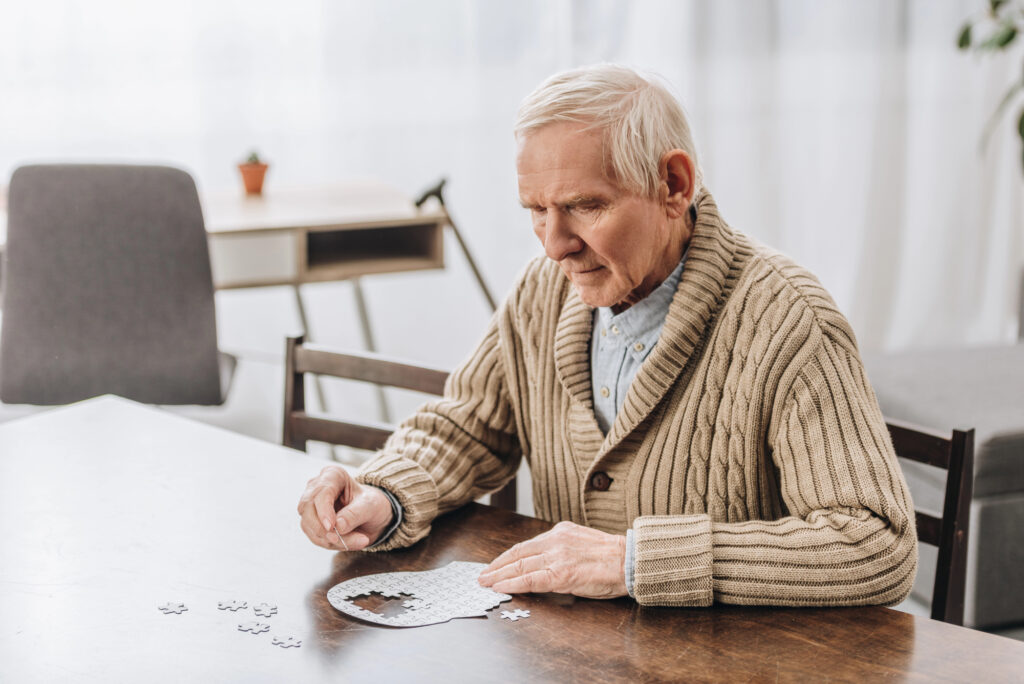 Geriatric man working on solving a puzzle of the outline of a human head