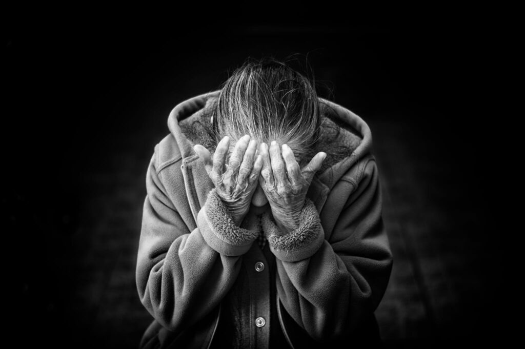 Black and white image of an elderly woman burying her hand into her hands grieving