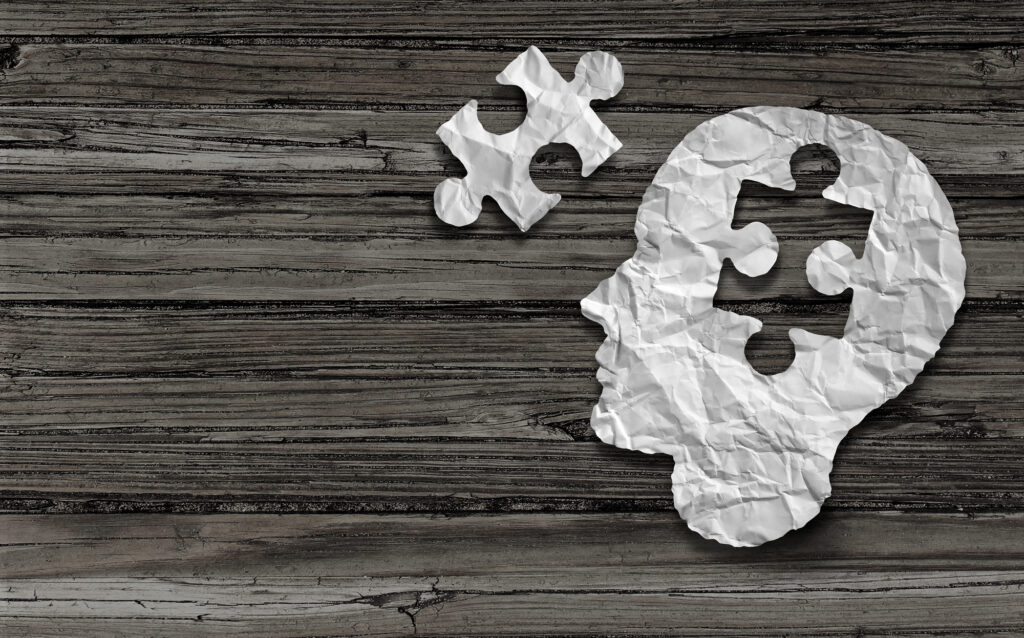 a puzzle piece taken out of white wrinkled cut out of the outline of a human head. A mental health puzzle