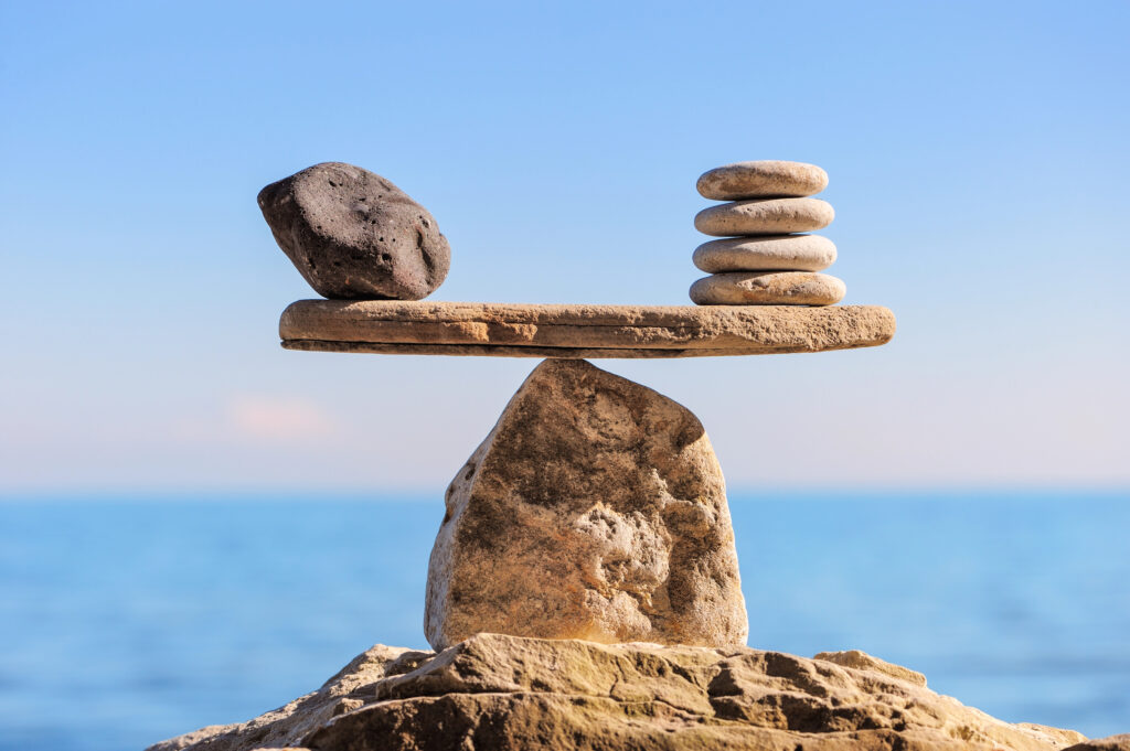 perfectly balanced stacked rocks vs a larger rock set on top of a large pointed rock as a scale. Representation of mindfulness and balance