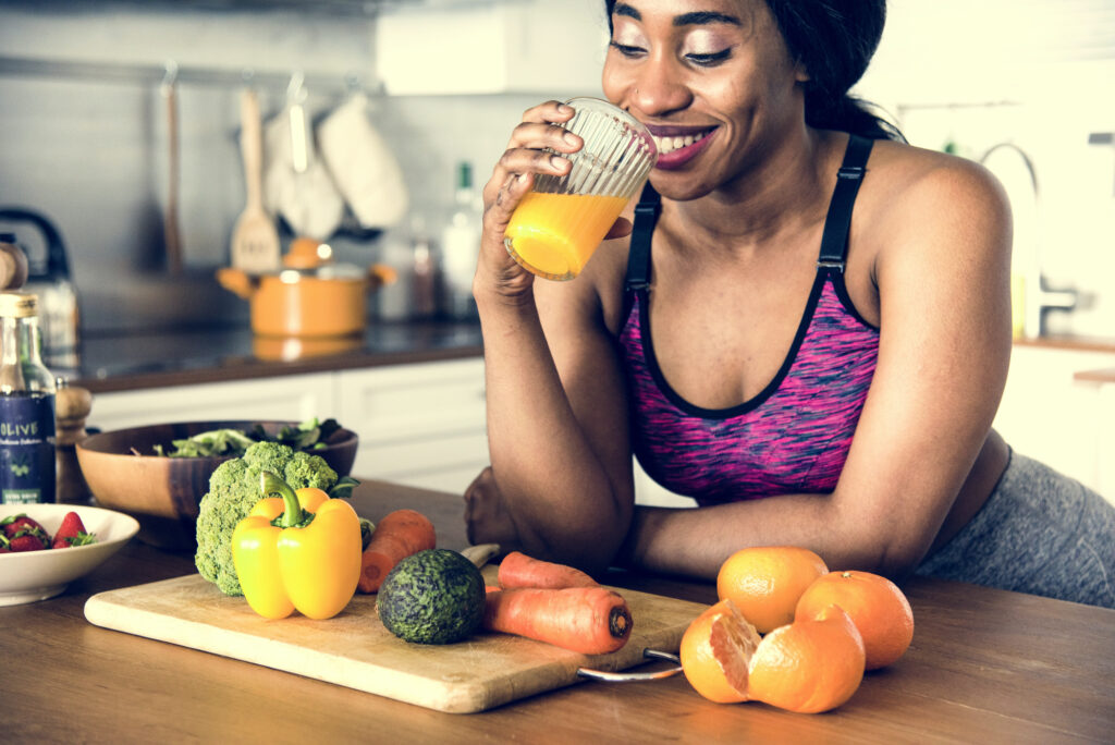 Black woman is drinking orange juice, surrounded by healthy food; healthy lifestyle and healthy nutrition