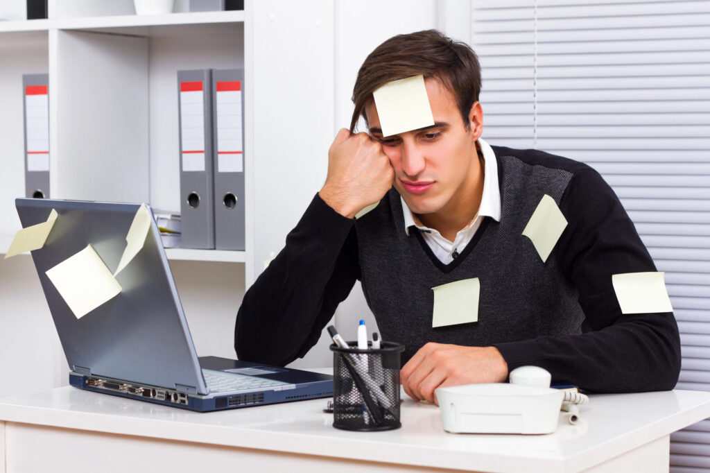 Man looks defeated at work covered in sticky notes
